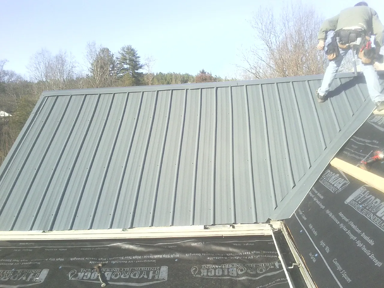 Crew installing dark green standing seam panels over synthetic underlayment in Carbondale
